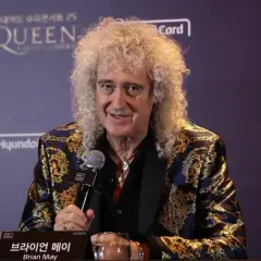 Brian May z zespołu Queen, w ozdobnej marynarce, udziela wywiadu.