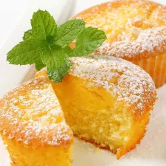 Två fluffiga citronmuffins, pudrade med florsocker och garnerade med mynta. Perfekt för ett enkelt citronmuffins recept.