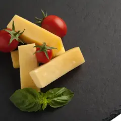 Pecorino co to? Kawałki żółtego sera, pomidorki koktajlowe i listki bazylii na ciemnej desce.