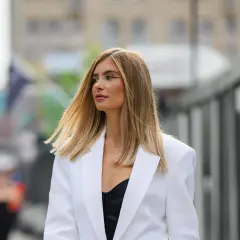 Frau mit blonden, leicht krisseligen Haaren nach Blondierung, trägt weißen Blazer und schwarzen BH.