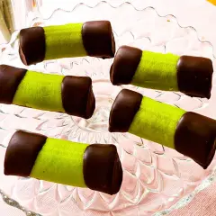 Fem gröna bakelser med chokladtoppar på ett glasfat. Som små dammsugare redo att avnjutas med en kopp kaffe.