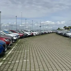 Duży plac z rzędami zaparkowanych samochodów pod zachmurzonym niebem.