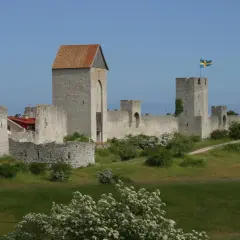 Visby muren reser sig stolt mot en blå himmel, med svenska flaggor som vajar från tornen. En historisk stadsvall som vittnar om svunna tider.