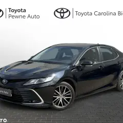 Elegancka, czarna Toyota Camry z napisem "Pewne Auto" na grillu. Lśniący lakier odbija światło, podkreślając dynamiczną sylwetkę sedana.