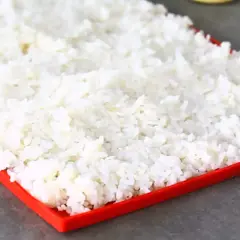 En stor mängd perfekt kokt **sushi ris** sprids ut på en röd bricka, redo att bli till läckra rullar.