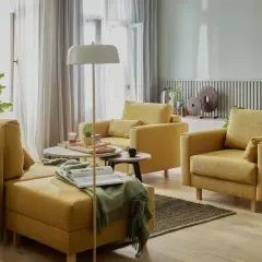 Przytulny salon bez telewizora. Żółte meble wypoczynkowe, stoliki kawowe, lampa podłogowa i mnóstwo zielonych roślin tworzą relaksującą atmosferę.