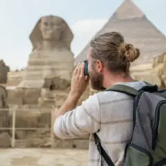 Hombre con mochila y cámara fotográfica admira la Esfinge y las pirámides. Es seguro viajar a Egipto y vivir esta experiencia.