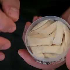 En hand håller en dosa med flera påsar. Det ser ut som fake snus, men det är svårt att säga säkert.