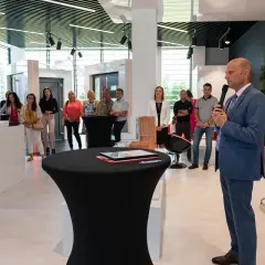 Mężczyzna w garniturze przemawia do grupy osób w nowoczesnym salonie okien i drzwi.
