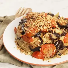 En läcker maklobe kyckling med aubergine, tomater och pinjenötter, serverad på en vit tallrik.