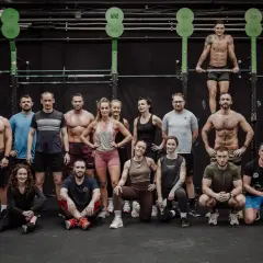 Grupa osób w strojach sportowych pozuje na tle sali treningowej CrossFit.