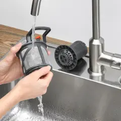 Czyszczenie zmywarki Electrolux. Ręce płuczą filtr pod bieżącą wodą w zlewie. Obok leży drugi, czysty filtr.