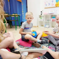 Dzieci siedzą na podłodze, bawiąc się zabawkami. To świetny sposób, jak uczyć dzieci angielskiego przez zabawę.