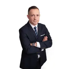 Mężczyzna w garniturze ze skrzyżowanymi rękami, na białym tle.