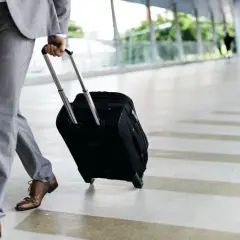 Mężczyzna w garniturze ciągnie walizkę na kółkach po nowoczesnym korytarzu.