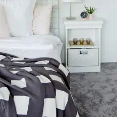 Un letto accogliente con coperta a quadri e un morbido tappeto grigio, perfetto per la posa moquette.