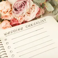 Bukiet róż i eukaliptusa obok notatnika z napisem "Wedding Checklist". Planowanie wesela w lesie zaczyna się od listy zadań.
