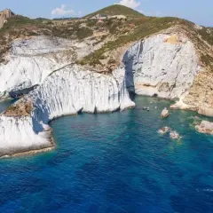 Scogliere bianche a picco sul mare blu intenso di Ponza. Un piccolo gozzo solca le acque cristalline, mentre la natura scolpisce la costa.