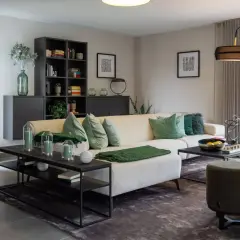 Modernes Wohnzimmer mit beigem Sofa, grünen Akzenten und hellgrauen Wänden. Diese Wandfarben sind modern und schaffen eine ruhige Atmosphäre.