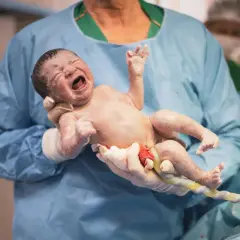 Noworodek z pępowiną, trzymany przez lekarza w rękawiczkach. To moment po porodzie, a nie sposób, jak wywołać poród.