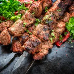 Soczysty kebab gruziński na metalowych szpikulcach, ozdobiony świeżą natką pietruszki i papryką.