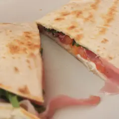 Pyszna piadina romagnola z szynką, pomidorami i rukolą, złożona na pół, gotowa do jedzenia.