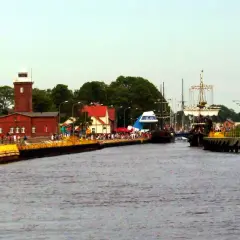 Widok na port z latarnią morską, statkami i ludźmi na nabrzeżu.