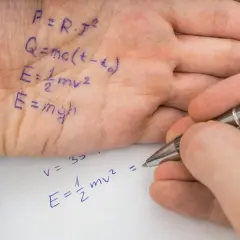 Wzory fizyczne zapisane na dłoni i na kartce papieru, obok długopisu.