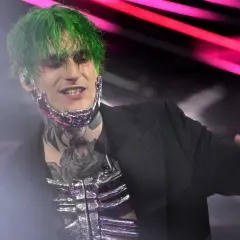 Theo la sad, con capelli verdi e trucco drammatico, indossa un abito nero e una maschera metallica.