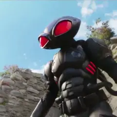 Czarny Manta z Aquaman 3 w zbroi, z czerwonymi oczami, stoi na tle kamiennych ruin i błękitnego nieba.