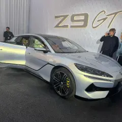 Srebrny Denza Z9 GT z otwartymi drzwiami, obok niego rozmawiają ludzie.