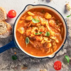 Herzhaftes Minestrone Rezept in einer blauen Pfanne, garniert mit Basilikum. Dazu gibt es knuspriges Brot und frische Tomaten.