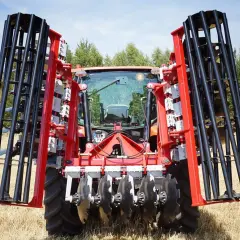 Czerwony traktor z zamontowanym agregatem do bronowania, gotowy do pracy na polu.