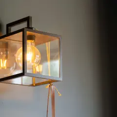 Aplique de foco con estructura metálica negra y cristal, iluminando con una bombilla de filamento.