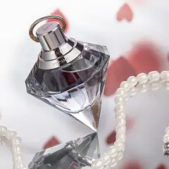 Luksusowy flakon ambperfumy Chopard Wish, otoczony perłami i serduszkami, symbolizuje elegancję i romantyzm.