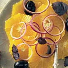 Erfrischender Salat mit Orangen, roten Zwiebelringen, schwarzen Oliven und dunklen Kräutern auf einem Teller.