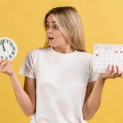 Zaskoczona kobieta trzyma zegar i kalendarz z serduszkami, zastanawiając się nad przyczynami braku okresu.