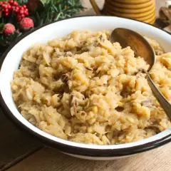 Pyszna kapusta kiszona z grzybami leśnymi, podana w misce, z łyżką. W tle świąteczne dekoracje.