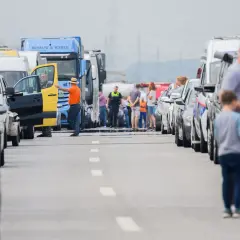 Stau auf der Autobahn. Ein Mann in orangefarbener Jacke und Hut steht neben einem gelb-schwarzen Transporter, dessen Tür offen ist. Viele Autos und LKW stehen still, als ob sie trotz Fahrverbot unterwegs wären.
