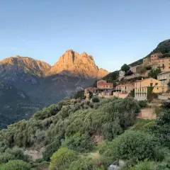 Village perché sur une colline, baigné par le soleil couchant. Les montagnes du nord, d'une difficulté certaine, se dressent en arrière-plan.