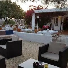 Mesas puestas en el exterior de un restaurante con un bar aguamarga. Ambiente tranquilo bajo la luz del atardecer.