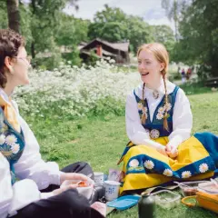 Två personer i folkdräkter njuter av en picknick under midsommar på Skansen.