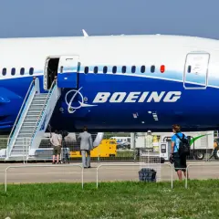 Ogromny samolot Dreamliner Boeing z otwartymi drzwiami i schodkami. W tle ludzie i sprzęt lotniskowy.