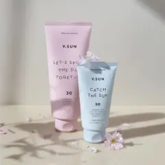 Zwei V.SUN Sonnencreme-Tuben, eine mit Lichtschutzfaktor 30 für den Körper, die andere mit LSF 50 für das Gesicht, umgeben von zarten Blütenblättern.