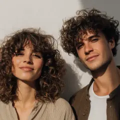 Ein junges Paar mit vollen Locken vor einer weißen Wand. Die curly girl lächelt sanft.