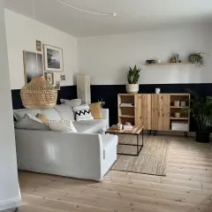 Salon moderne avec canapé gris, meuble en bois et tapis en jute. Le mur est peint en deux tons, blanc et bleu nuit, rappelant des techniques de peinture acrylique.
