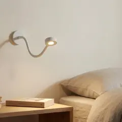 Biała, elastyczna lampa nocna oświetla stos książek na stoliku obok łóżka.