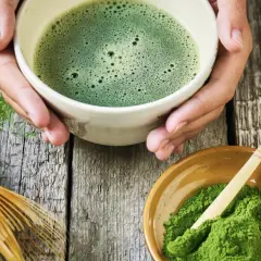 Zielone, spienione napój w miseczce, obok proszek i bambusowa miotełka. Tak przygotowuje się co to matcha.