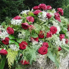 Bogactwo czerwonych róż i drobnych białych kwiatów tworzy elegancki wieniec pogrzebowy, symbolizujący pamięć i szacunek.