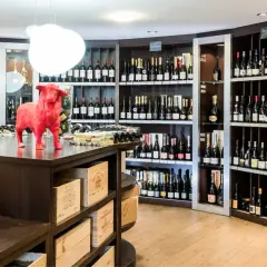 Une cave à vin bien garnie, avec une statue de taureau rouge au centre. Des bouteilles de champagne et de vin sont exposées sur des étagères.